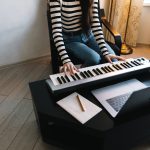 Young caucasian woman learns to play the piano keys using a laptop at home distantly.